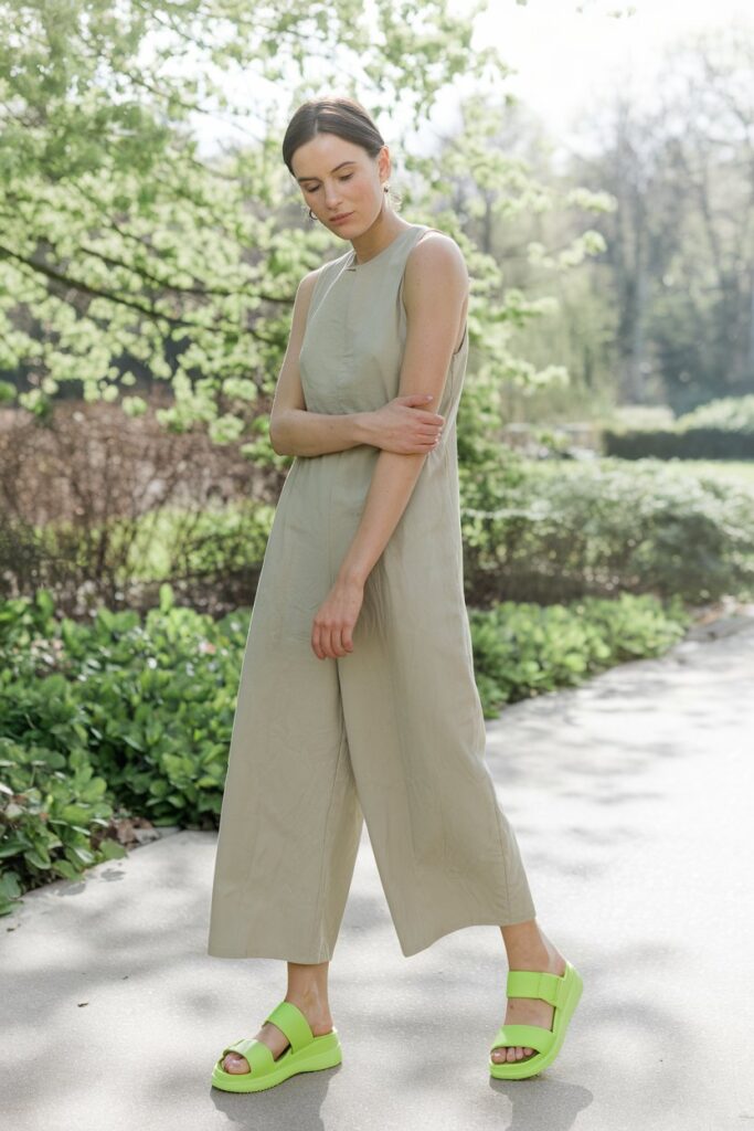 woman outdoors on a bright spring afternoon, wearing a soft beige jumpsuit with neon sandals that burst with color.