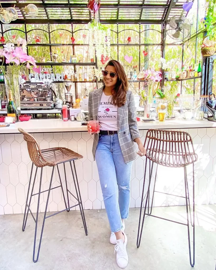 Woman wearing blazer, graphic tee, light jeans, and white sneakers – casual Friday office outfit