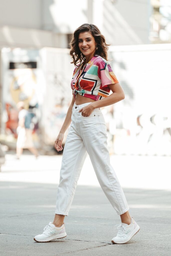 Trendy girl in bright printed top tucked into white jeans, paired with clean tennis shoes