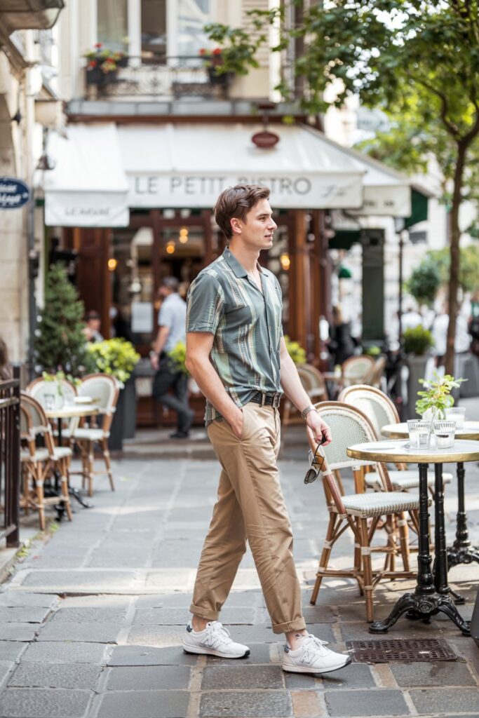 A male model heading into a restaurant patio or brunch spot, wearing classic khakis, untucked patterned short-sleeve shirt, and clean white NB 574s.