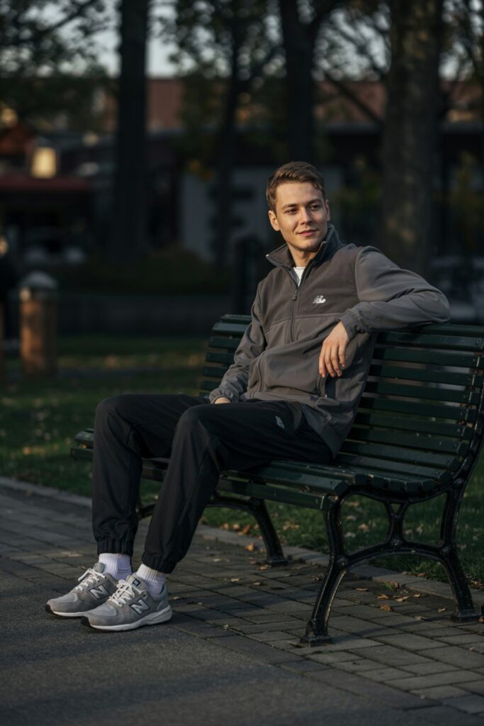Male model lounging on a park bench or leaning against a wall in a zip-up fleece