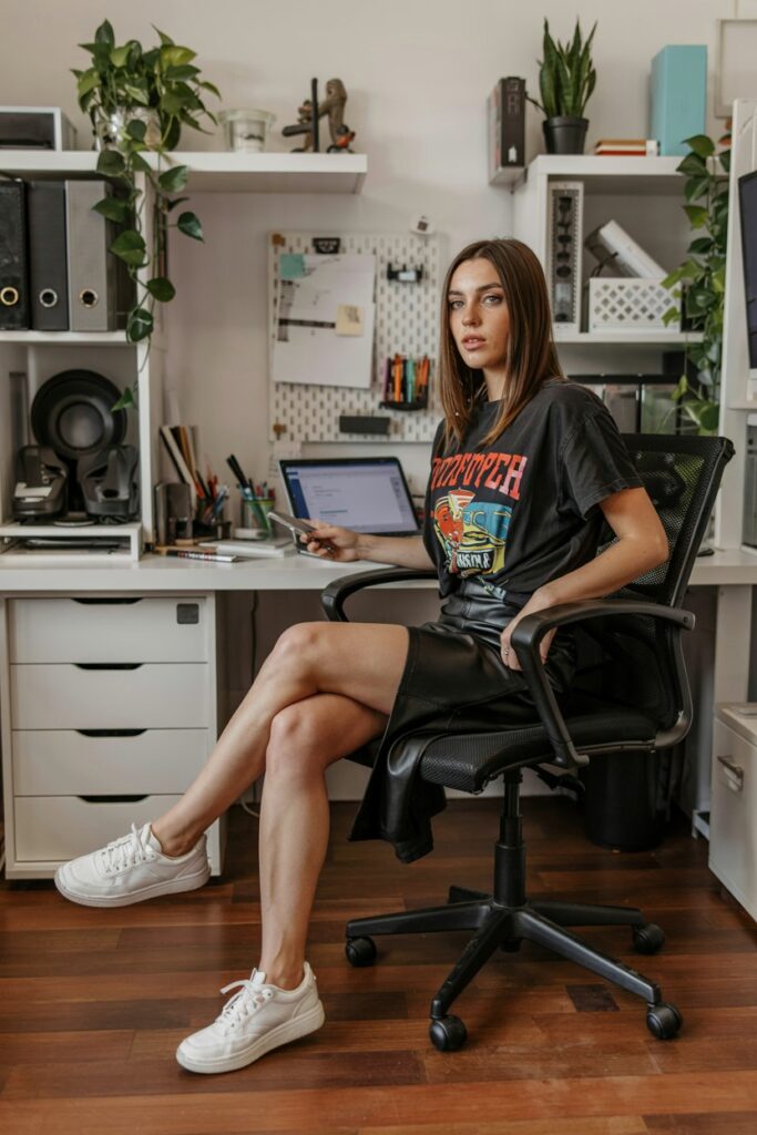 Trendy girl in a black pencil skirt, tucked-in graphic tee, and clean white tennis shoes, sitting at her desk