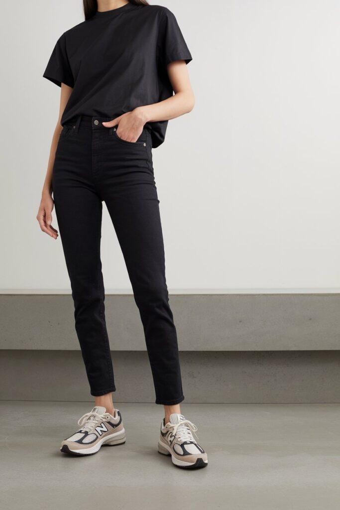 A woman dressed in black slim jeans and a matching black tee, accented by monochrome New Balance sneakers