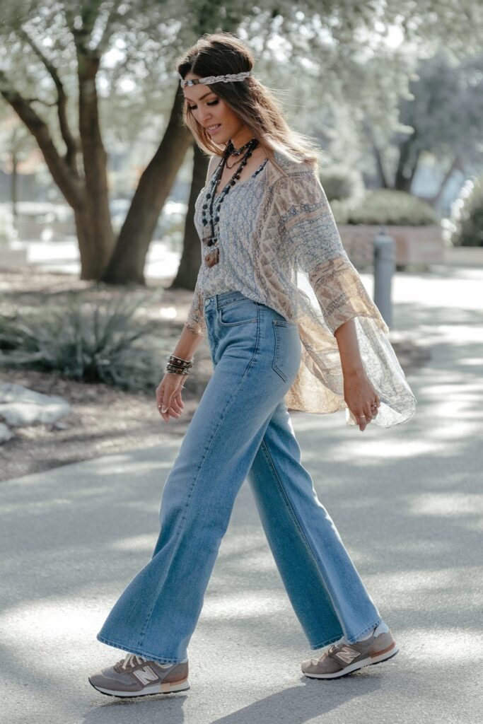 "A woman in flared, relaxed-fit jeans and a patterned, flowy top paired with vintage-style New Balance sneakers
