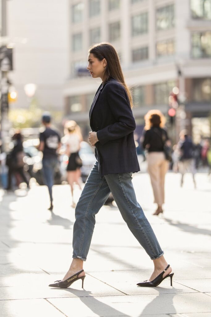 Trendy woman in cropped jeans and a blazer, walking confidently in sleek black slingback kitten heels
