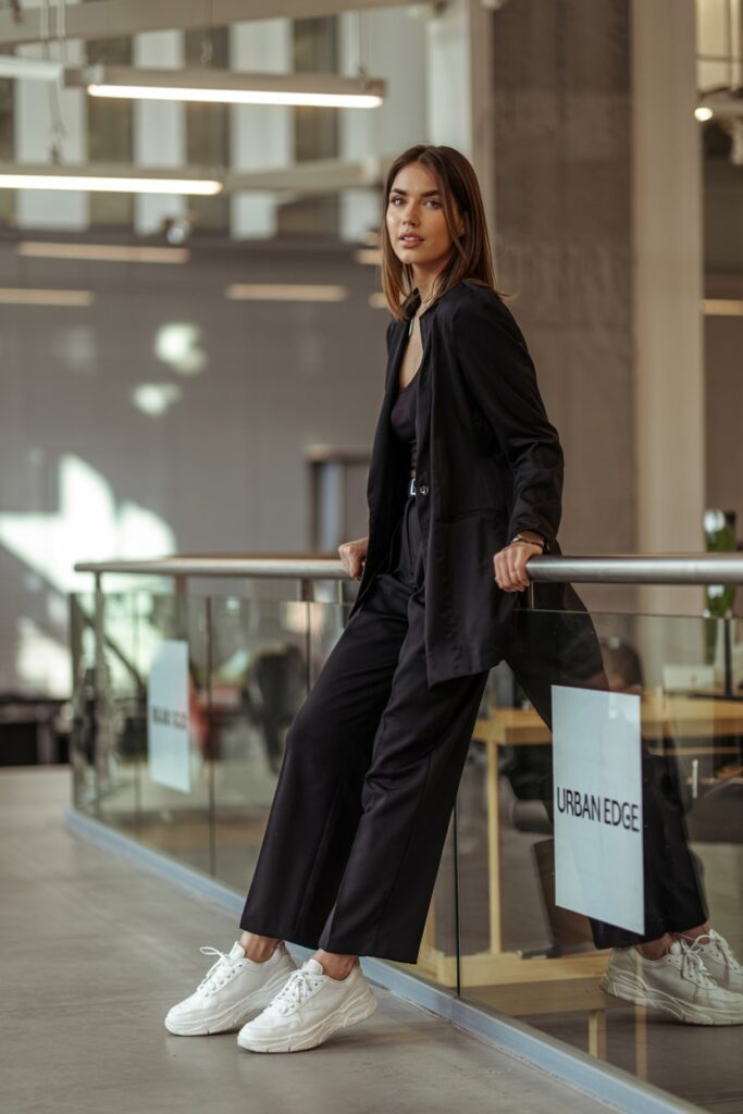 Trendy girl in an all-black monochrome outfit with bold statement sneakers, leaning casually on a railing in an office space