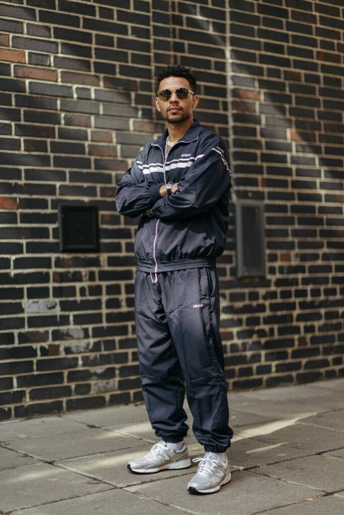A man in a full matching 90s-style tracksuit in navy or burgundy, wearing silver NB 530s.