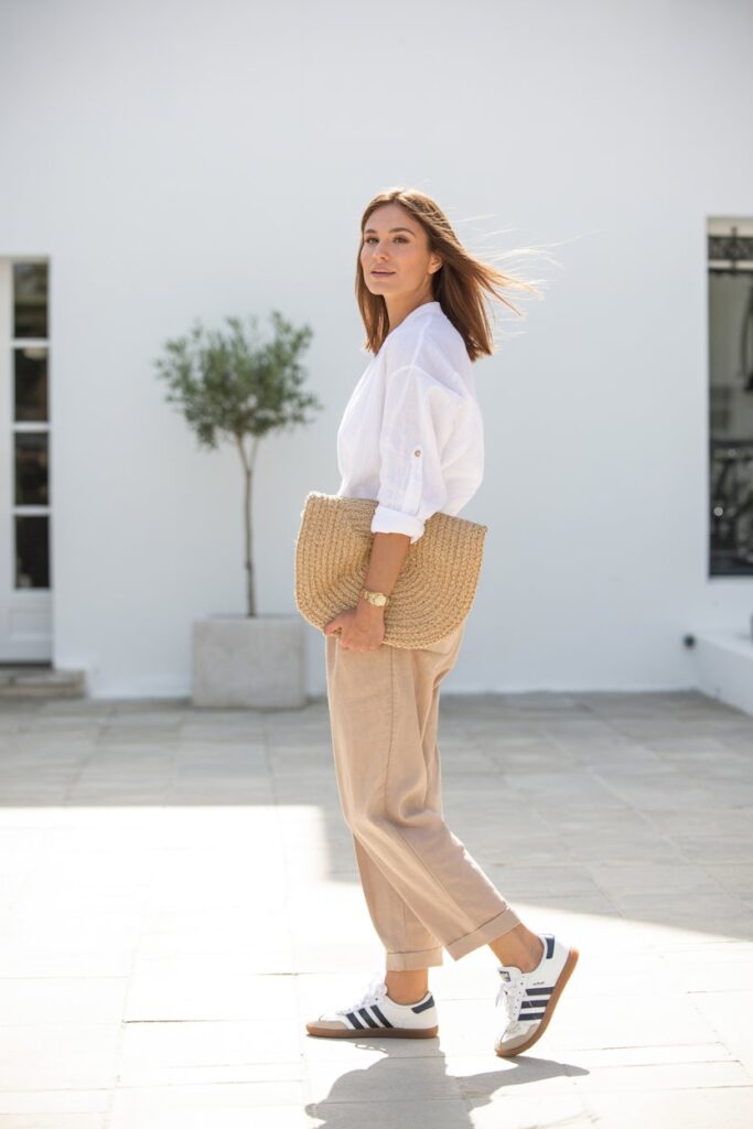 A woman in linen pants, a white blouse, and white Adidas Sambas exudes minimalist summer chic