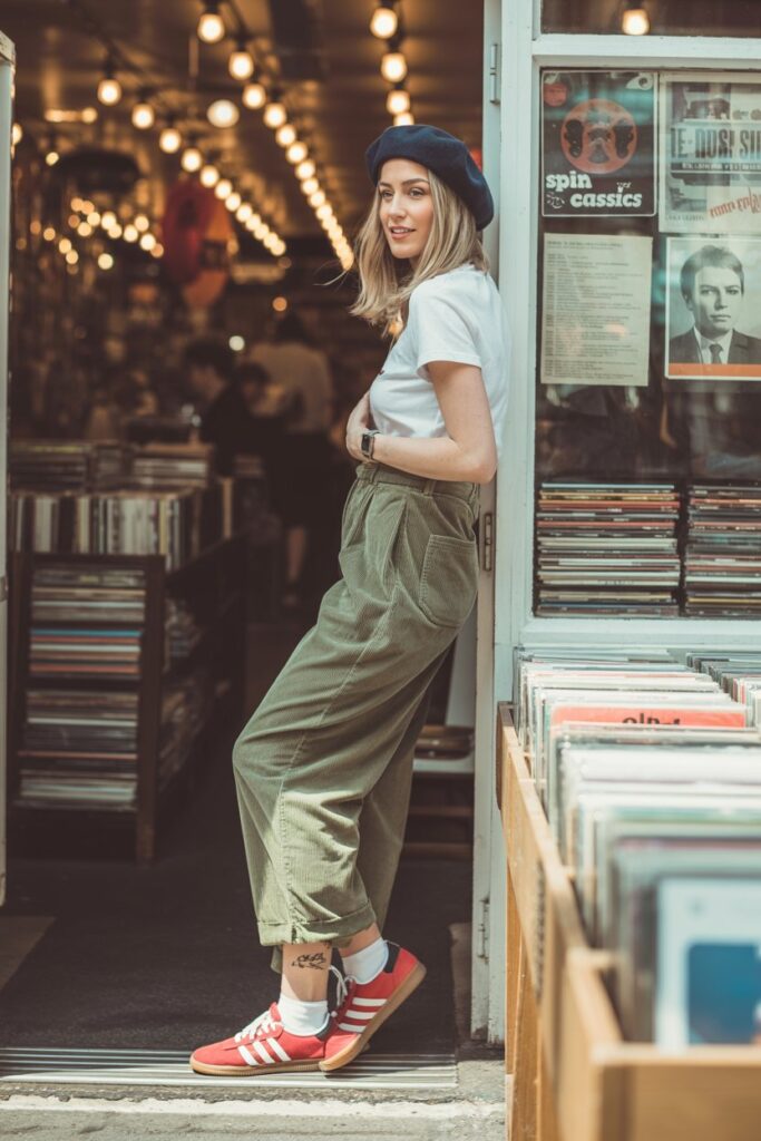 A woman in corduroy pants, a tee, and red Adidas Sambas channels retro street flair.