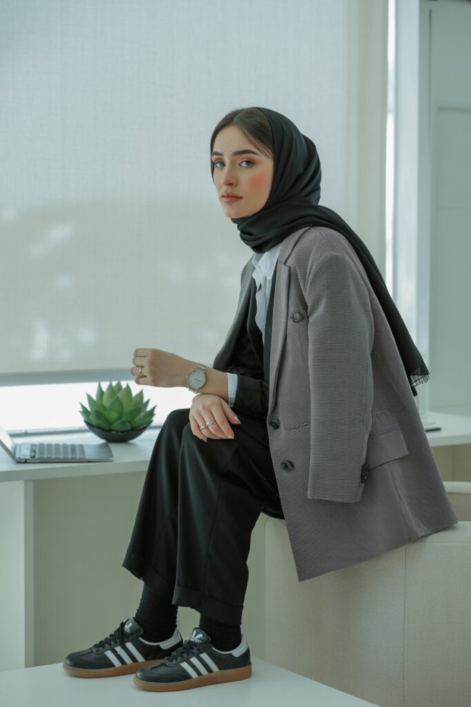 A woman in a black hijab, gray blazer, trousers, and black Adidas Sambas rocks urban chic.