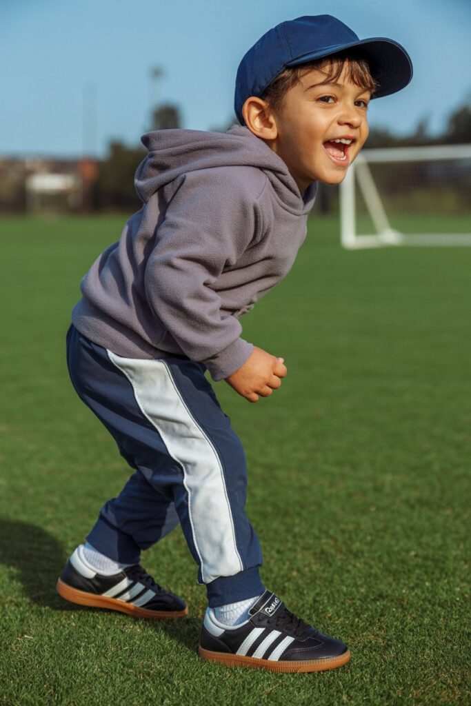 A child in track pants, a hoodie, and black Adidas Sambas shines in a sporty kids’ look.