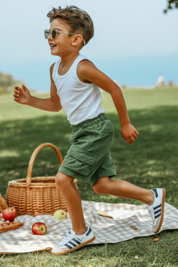A child in cargo shorts, a tank, and white Adidas Sambas shines in a summery kids’ outfit.