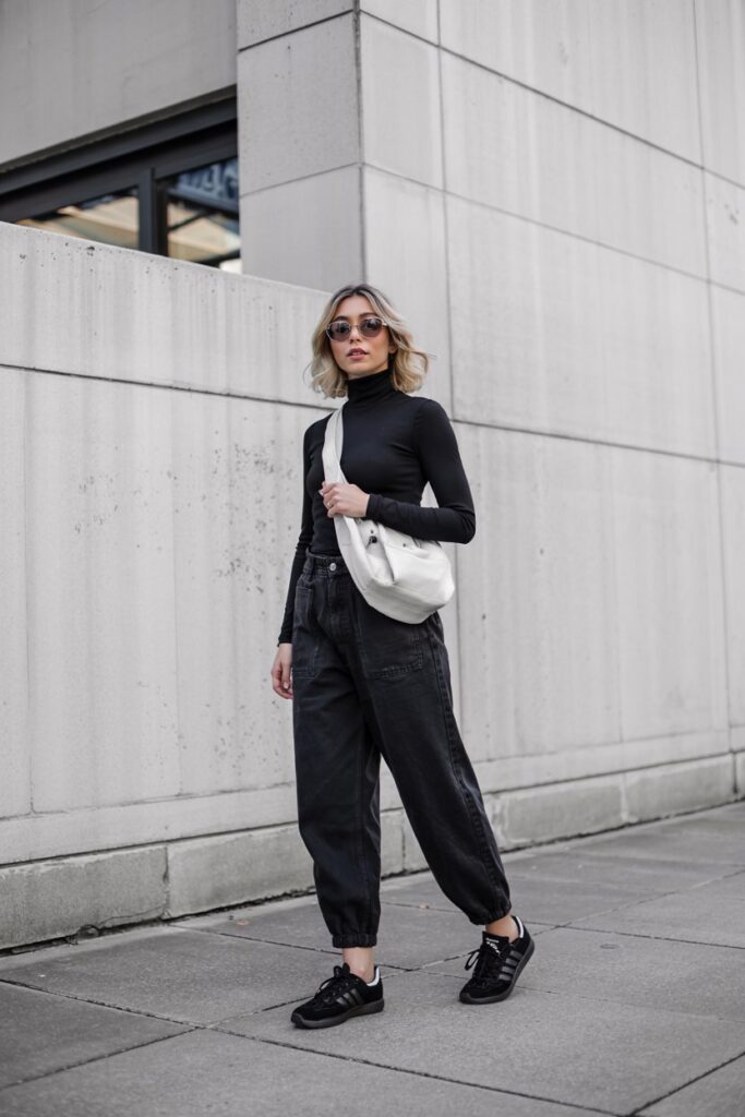 Modern woman in an all-black outfit: fitted black turtleneck, onyx baggy jeans, and black Adidas Sambas, 