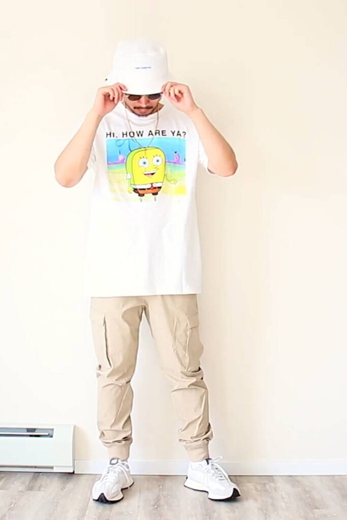 White cartoon graphic tee + beige cargo joggers + white NB 327 + white cap + silver chain