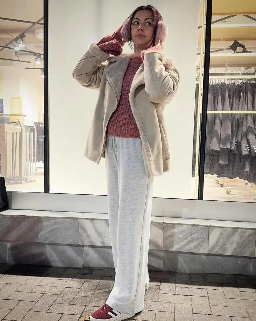 shearling jacket layered over a textured mauve knit sweater and loose-fitting light grey pants. Complete the look with maroon Gazelle Bolds